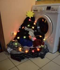 Pile of laundry by a washing machine, decorated with lights and star to look like a Christmas tree. Festive fashion if you're plus-size & pregnant
