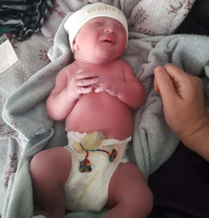 Newborn baby with rainbow cord tie in nappy and hat
