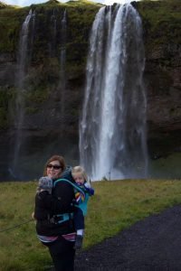 Sian carries a sleeping toddler on her back in an Isara carrier in front of a waterfall