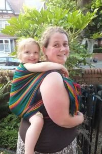 Amber carrying a toddler in a rainbow coloured woven wrap