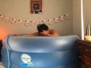 Amy's home waterbirth - Amy in her pool, looking down, hand to her head.