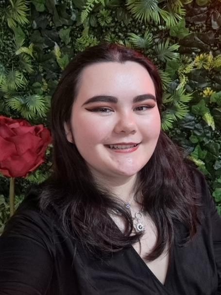 Picture of Hannah Allen who is stood in front of a wall of foliage. She has shoulder length brown hair and is smiling.