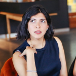 Image of Manna Mostaghim, who has her hair in a short black bob, wearing a simple black dress and looking off camera.